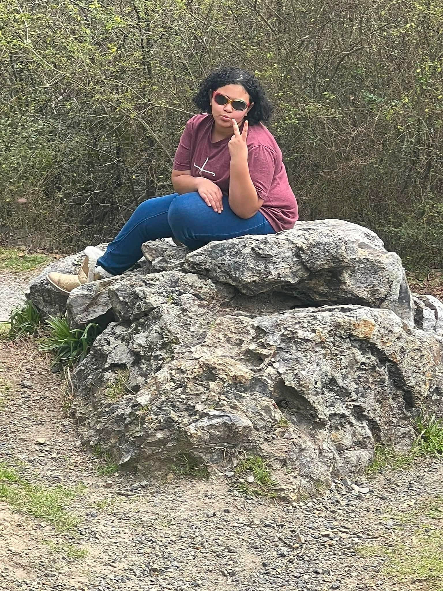 Ashlynn joined the competition — help win amazing prizes! bedrock, forest, grass, headwear, human_leg, knee, landscape, leisure, luggage_and_bags, natural_landscape, outcrop, people_in_nature, person, plant, recreation, rock, sitting, soil, sunglasses, thigh