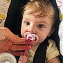 baby, infant, pacifier, car_seat, warning_label, seat_belt, hand, close_up, portrait, eyes, face, hair, bottle, pacifier_clip, clothing, strap, buckle, skin, sitting, cute