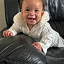 Khalesei is registered to the contest to win money with this photo: baby, black_leather_couch, child, cozy, crawling, cute, expression, fur_collar, furniture, hair_bow, happy, indoor, infant, person, playful, portrait, smiling, texture, white_clothing, young_child