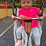 toddler, child, swing, playground, pink_shirt, bow, blanket, outdoor, park, fence, grass, cloudy_sky, holding, metal_bar, socks, leggings, happy, smiling, curly_hair, daytime