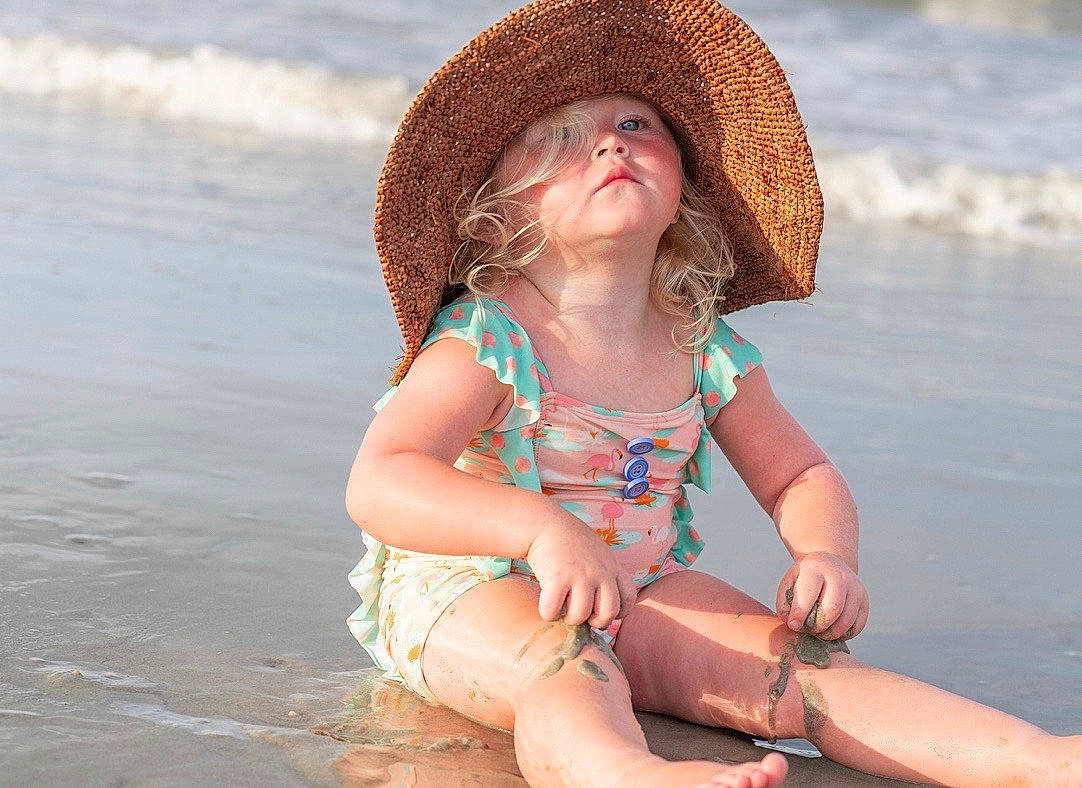Riley is registered to the contest to win money with this photo: azure, baby_toddler_clothing, beach, eye, face, facial_expression, hairstyle, happy, hat, head, headgear, leg, people_in_nature, people_on_beach, person, skin, sun_hat, textile, thigh, toddler
