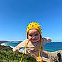 Daniela is registered to the contest to win money with this photo: baby, child, yellow_hat, person, outdoor, beach, ocean, sky, blue_sky, tattoo, hand, watch, nature, greenery, coastline, sunny, smile, playing, cute, portrait