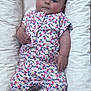 baby, infant, child, cushion, floral_outfit, socks, polka_dots, bed, pillow, cute, lying_down, looking_at_camera, soft_lighting, indoor, comfortable, small_animal_pattern, pink, white, colorful, calm