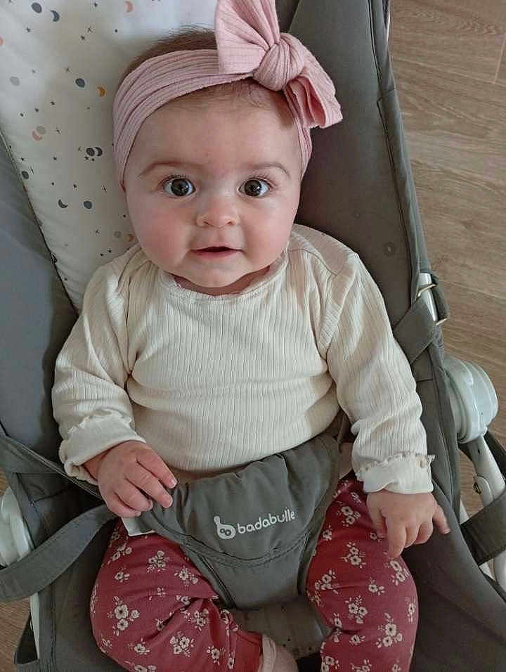 Athéna participe au concours pour gagner de l'argent avec cette photo : baby, infant, child, headband, pink_bow, baby_bouncer, cream_top, floral_pants, wide_eyes, cute, indoor, flooring, seated, portrait, looking_at_camera, clothing, infant_clothing, face, expression, comfort