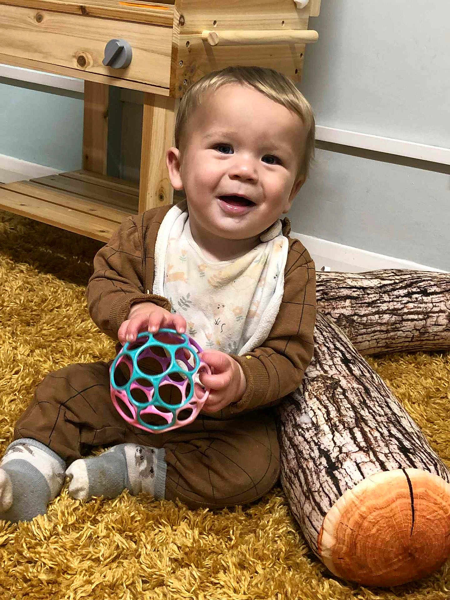 Brayden joined the competition — help win amazing prizes! toddler, child, smiling, toy, ball, pajamas, socks, carpet, floor, cushion, log_pattern, wooden_furniture, indoor, baby, cute, playful, happy, person, home, cozy