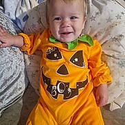 Brayden is registered to the contest to win money with this photo: baby, child, pumpkin_costume, orange_clothing, smiling, face, cushion, blanket, indoor, cozy, cute, holiday, festive, halloween, infant, person, apparel, head, happy, toddler