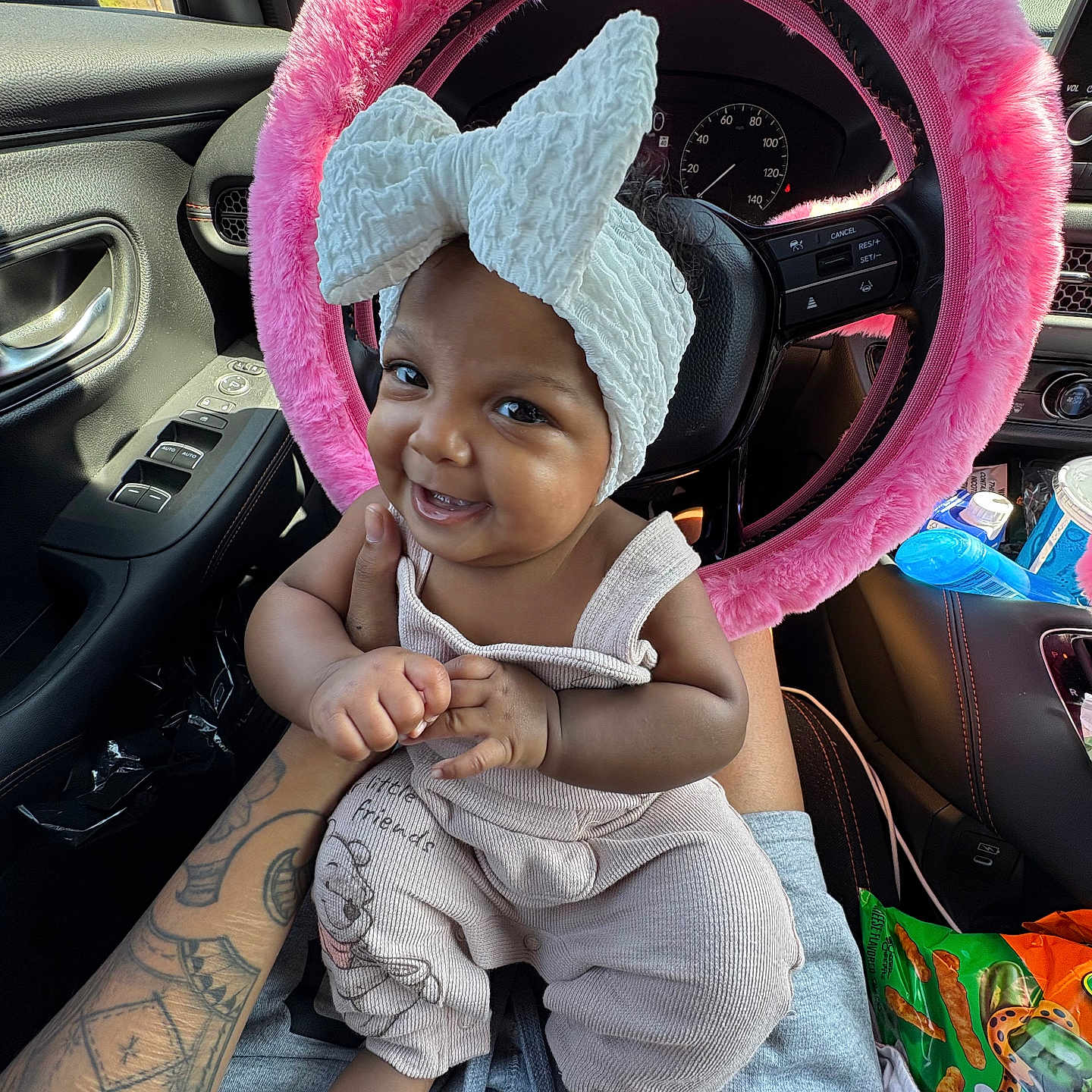 Aulelei is registered to the contest to win money with this photo: baby, bow, car_interior, child, clothing, daylight, foot, fuzzy, hand, happy, headband, overalls, person, pink, seat, smile, snack, steering_wheel, tattoo, window