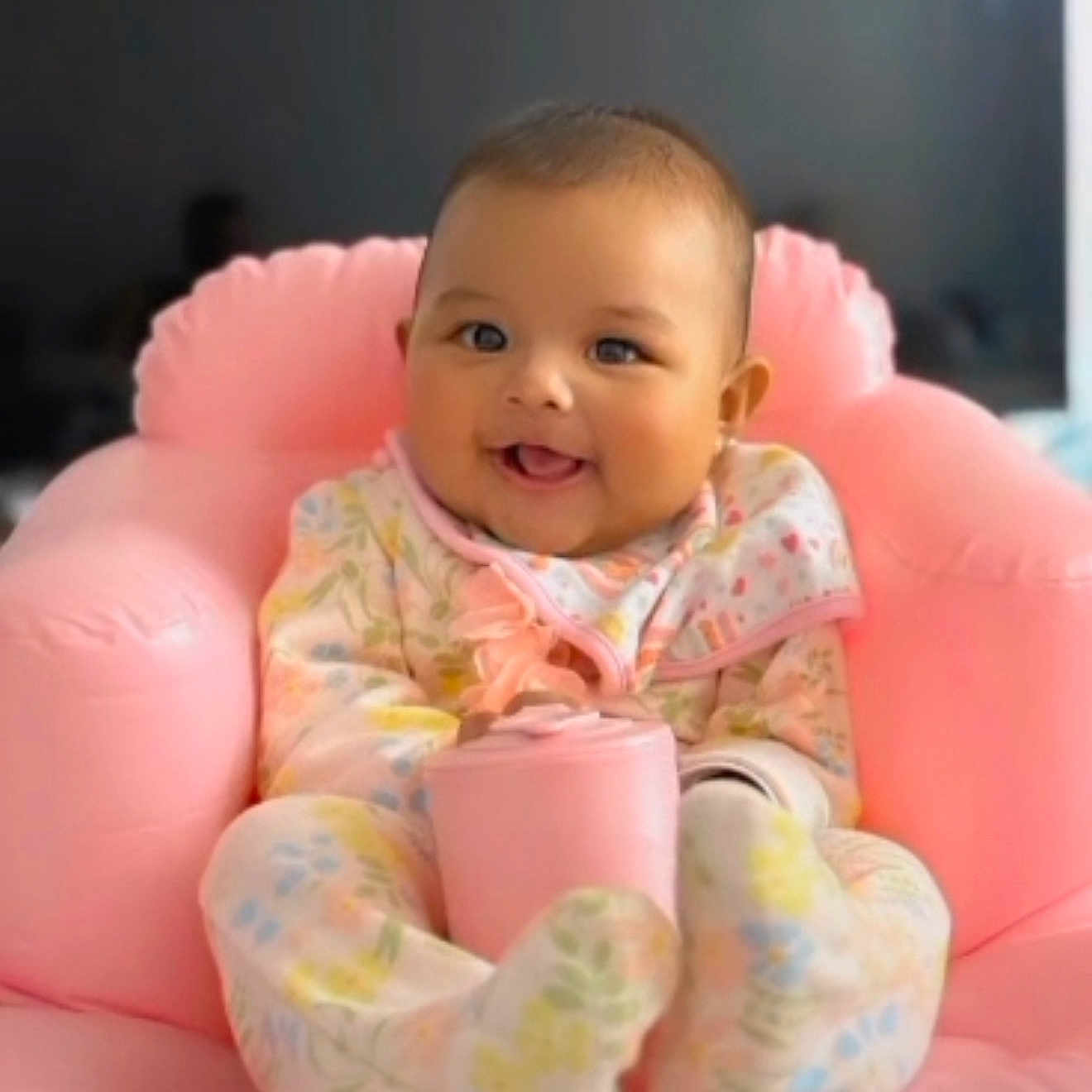 Sophie is registered to the contest to win money with this photo: baby, child, comfort, cozy, cup, cute, expression, face, floral_pattern, furniture, happy, home, indoors, infant, onesie, pink_chair, portrait, seated, smiling, soft_texture