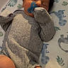 baby, sleeping, pacifier, gray_clothing, black_cap, blanket, patterned_sheet, infant, peaceful, indoors, soft_lighting, resting, cute, newborn, child, cozy, small, person, wrapped, toddler