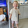 Scarlett is registered to the contest to win money with this photo: child, girl, smile, happy, indoor, kitchen, tshirt, bunny, shorts, sneakers, carpet, floor, cabinet, window, water_bottle, television, furniture, person, portrait, footwear