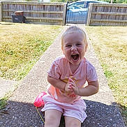 Scarlett joined the competition — help win amazing prizes! toddler, child, smiling, happy, outdoor, garden, grass, fence, toy, phone, playing, sunny, daylight, casual_clothing, shorts, tshirt, sitting, pathway, car, nature