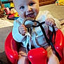 baby, smiling, red_baby_seat, toy, wooden_ring, ribbons, living_room, carpet, furniture, colorful_storage, child, happy, cute, infant, person, indoor, playful, blue_eyes, white_clothing, legs