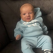 Tommy joined the competition — help win amazing prizes! baby, child, infant, hoodie, blue_clothing, socks, striped_socks, smiling, couch, indoor, seated, cute, young_child, portrait, person, comfortable, casual_clothing, relaxed, home, soft_lighting
