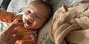 Tommy joined the competition — help win amazing prizes! baby, smiling, infant, onesie, orange_clothing, halloween_theme, ghost_print, pumpkin_print, bed, blanket, hand, tickling, happy, lying_down, face, person, indoors, cozy, cute, playful