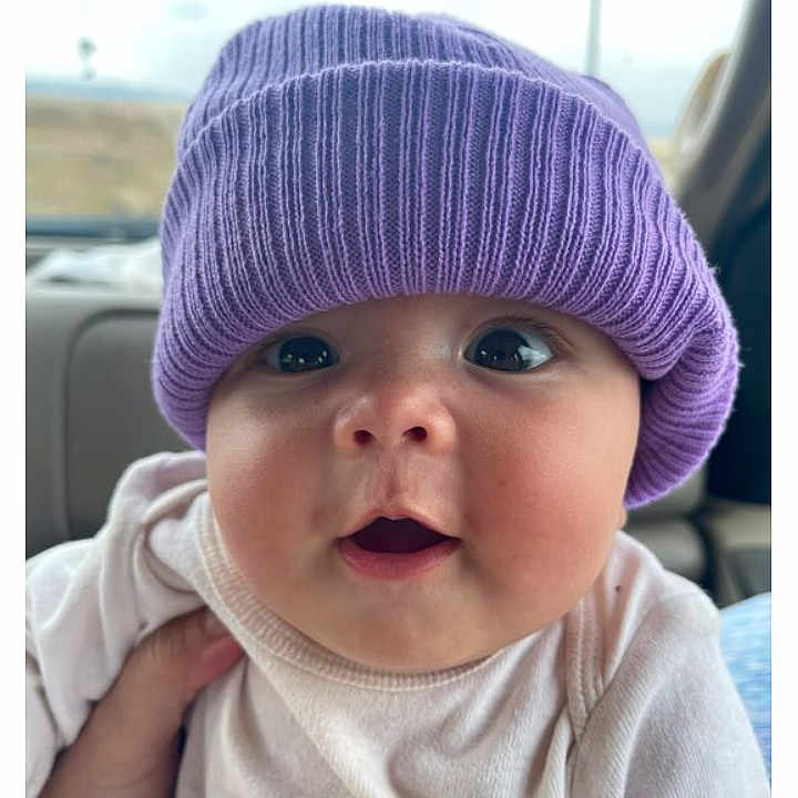 Charity is registered to the contest to win money with this photo: baby, beanie, bonnet, cap, clothing, cushion, face, hat, head, homedecor, newborn, person, photography, portrait, purple