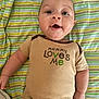 baby, infant, onesie, clothing, striped_blanket, smiling, happy, lying_down, child, cute, face, portrait, toddler, expression, skin, arm, hand, head, eyes, mouth