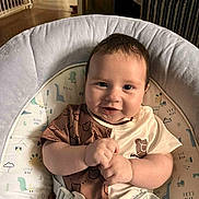 Aston is registered to the contest to win money with this photo: baby, infant, smiling, baby_seat, dinosaur_print, brown_clothing, beige_clothing, cushion, indoor, child, cute, happy, plush, straps, portrait, small_hands, face, eyes, hair, seat