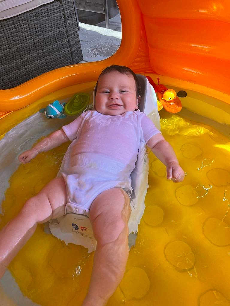 Aston is registered to the contest to win money with this photo: baby, infant, smiling, water, inflatable_pool, yellow, onesie, toy, bath_toy, child, happy, summer, outdoor, seat, plastic, reflection, skin, arm, face, leg