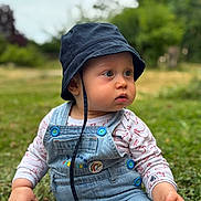 Morgan participe au concours pour gagner de l'argent avec cette photo : baby, child, denim_overall, bucket_hat, outdoor, grass, wooden_stick, curious, sitting, nature, greenery, portrait, cute, young_child, casual_clothing, daylight, blue_buttons, closeup, infant, expression