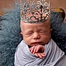newborn, baby, crown, sleeping, wrapped, blanket, portrait, closeup, soft_texture, blue, gray, peaceful, infant, cute, resting, headwear, fuzzy, comfortable, indoors, decorative