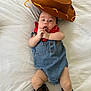 adorable, baby, bandana, boots, child, clothing, cowboy_hat, cute, denim_overalls, expression, fashion, footwear, hands, headwear, indoor, infant, lying_down, person, portrait, white_sheet
