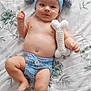 baby, infant, crochet_hat, crochet_diaper, toy, bone_toy, lying_down, bedspread, floral_pattern, cute, child, smiling, blue, handmade, soft_toy, indoor, person, headwear, clothing, skin