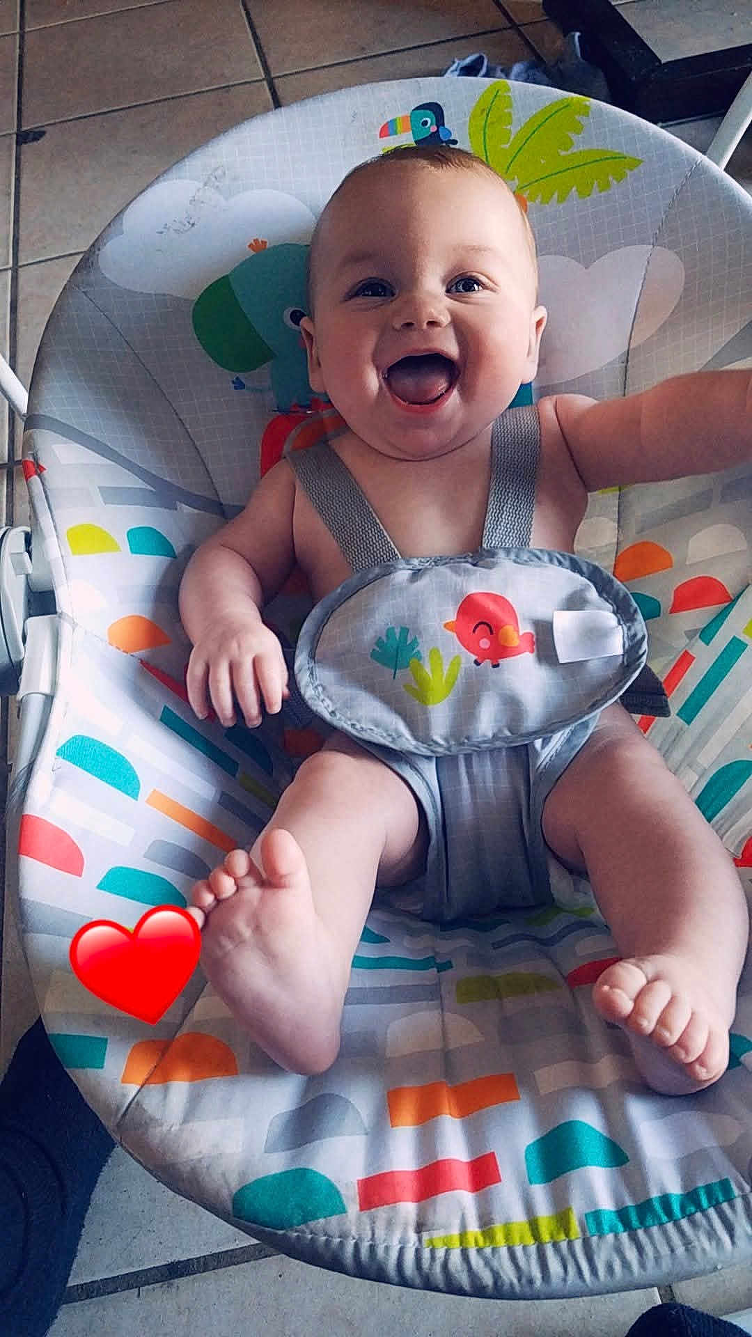 Liam joined the competition — help win amazing prizes! baby, child, smiling, happy, infant, baby_rocker, seat, colorful, patterned, animal_print, indoor, floor_tiles, foot, hand, person, cute, joyful, baby_clothing, strap, playful