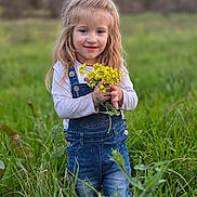 Oakley Young joined the competition — help win amazing prizes! casual_clothing, child, cute, daylight, denim_overalls, field, flowers, girl, grass, green, long_hair, nature, outdoor, plants, portrait, scenery, smile, standing, yellow, young