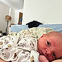 baby, newborn, infant, bed, pillow, blanket, onesie, animal_print, face, person, indoor, furniture, headboard, curious, gaze, soft_lighting, closeup, lying_down, cute, cozy