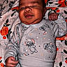 baby, infant, smiling, onesie, cartoon_characters, blanket, floral_pattern, sleepwear, cute, chubby_cheeks, lying_down, hand, face, head, indoors, child, newborn, soft_lighting, cozy, portrait