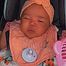 baby, infant, car_seat, headband, pacifier, blanket, floral_pattern, clothing, pink, orange, face, person, child, cute, sleepy, indoors, seat, accessory, comfort, toddler