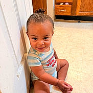 Daxyn Dereck is registered to the contest to win money with this photo: baby, casual, child, cute, floor, floor_tile, hair_bun, happy, indoor, kitchen, light_skin, onesie, person, playful, sitting, smiling, striped_clothing, toddler, wooden_cabinets, young_child