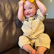 Kinsley is registered to the contest to win money with this photo: baby, child, smiling, sitting, couch, leather, headband, blue_eyes, clothing, happy, indoors, person, cute, infant, playful, portrait, hands, feet, fabric, furniture
