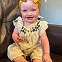 baby, child, smiling, blue_eyes, yellow_bow, headband, cream_outfit, floral_embroidery, sitting, couch, leather, indoor, happy, cute, infant, person, portrait, hand, foot, skin