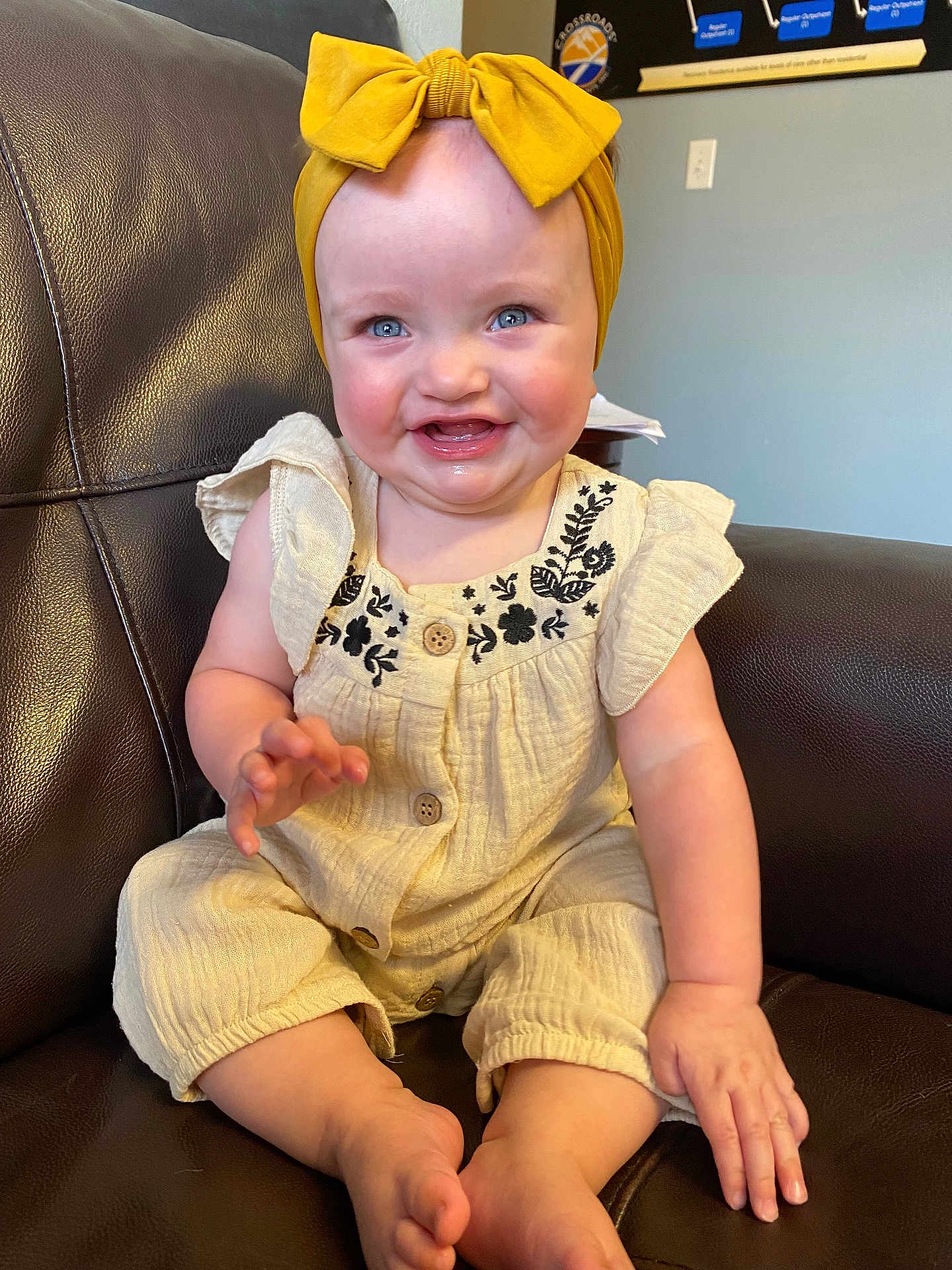 Kinsley is registered to the contest to win money with this photo: baby, child, smiling, blue_eyes, yellow_bow, headband, cream_outfit, floral_embroidery, sitting, couch, leather, indoor, happy, cute, infant, person, portrait, hand, foot, skin