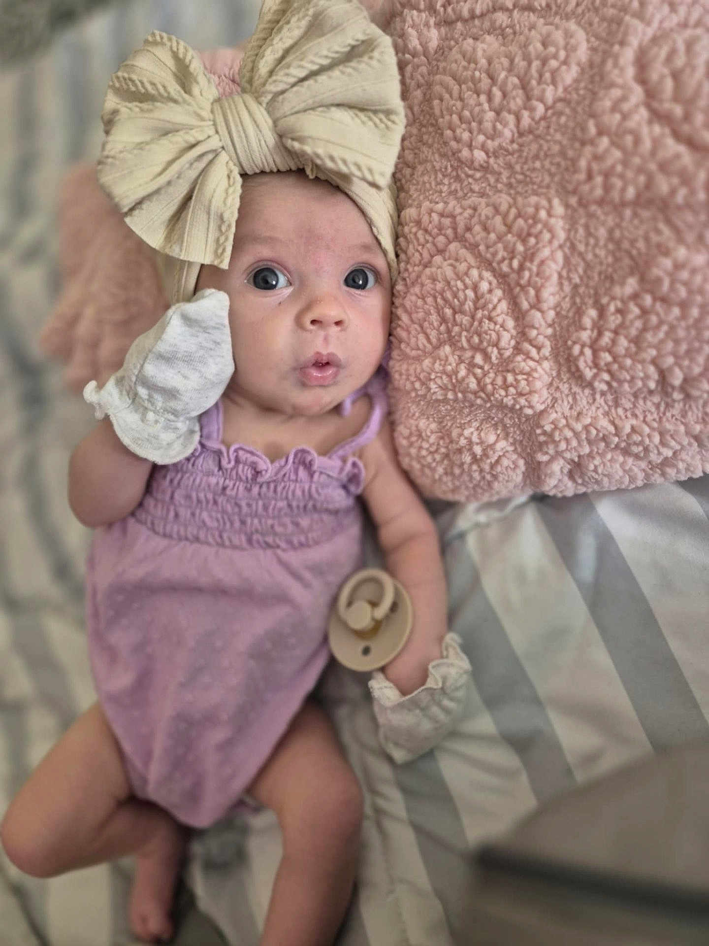 Oaklynn joined the competition — help win amazing prizes! baby, infant, headband, bow, mittens, pacifier, blanket, pink, purple_clothing, bed, striped_bedding, soft_texture, cute, portrait, lying_down, wide_eyes, curious_expression, indoors, child, newborn