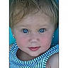 blue_eyes, child, close_up, date_display, digital_interface, earrings, expression, face, head_and_shoulders, indoors, light_hair, looking_at_camera, person, phone_screen, portrait, skin, sleeveless_top, striped_clothing, time_display, young_child