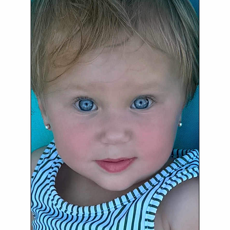Jillian is registered to the contest to win money with this photo: blue_eyes, child, close_up, date_display, digital_interface, earrings, expression, face, head_and_shoulders, indoors, light_hair, looking_at_camera, person, phone_screen, portrait, skin, sleeveless_top, striped_clothing, time_display, young_child