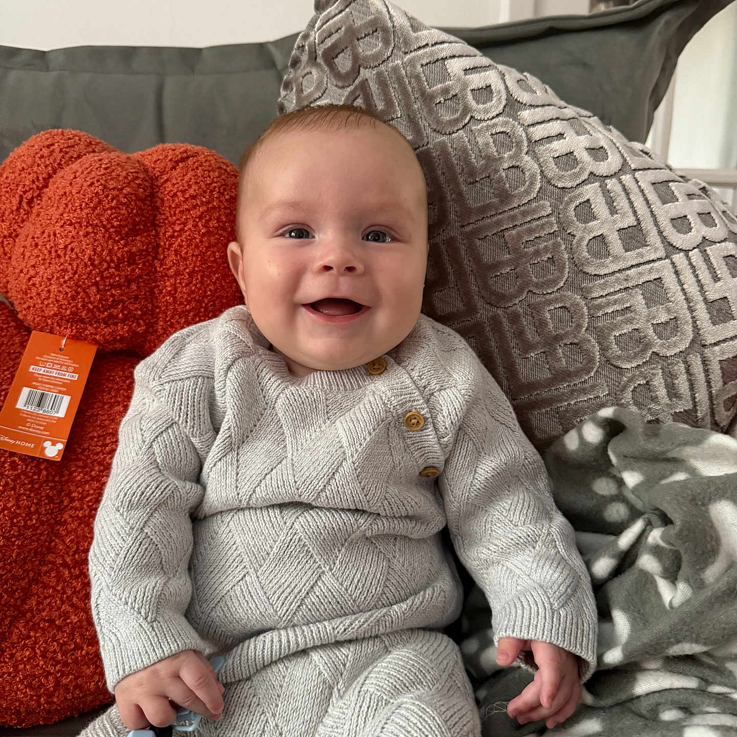 Lennox is registered to the contest to win money with this photo: baby, blanket, button, child, comfort, couch, cozy, cushion, face, hand, happy, home, indoor, knitted_clothing, pattern, person, plush, sitting, smile, toy