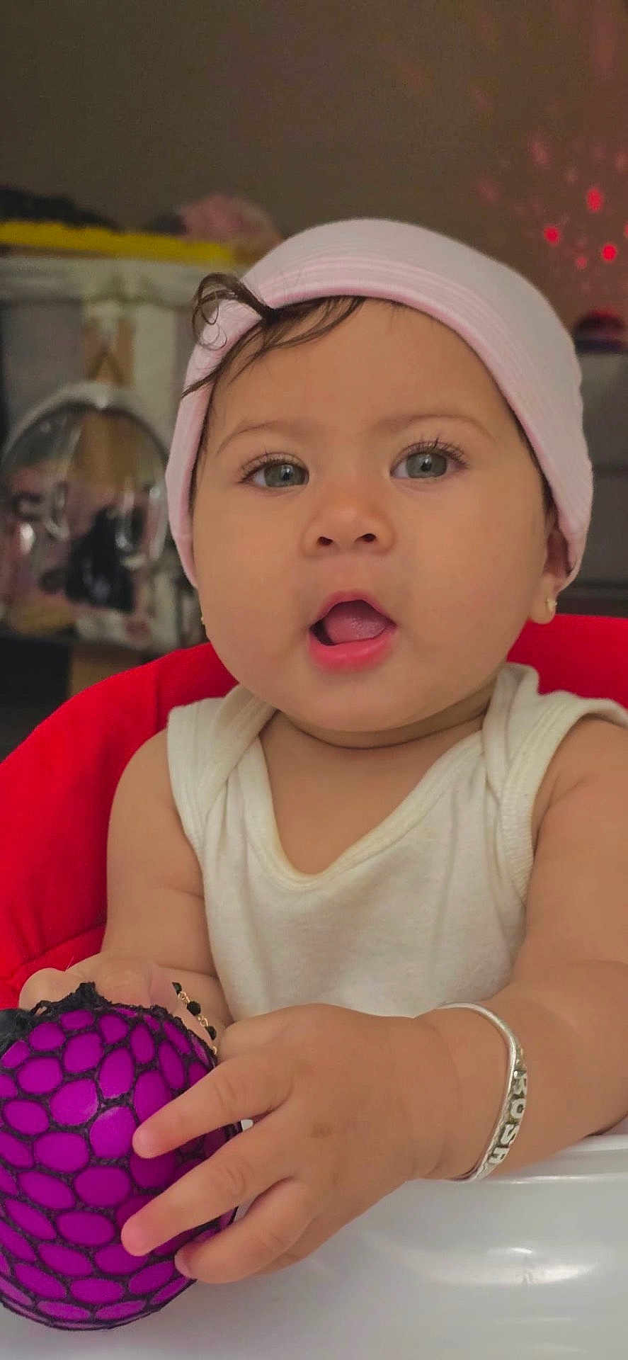 Rosa joined the competition — help win amazing prizes! baby, ball, bracelet, child, curly_hair, cute, expression, face, hand, hat, indoor, pink, playful, portrait, red_chair, sitting, skin, toy, white_tank_top, young