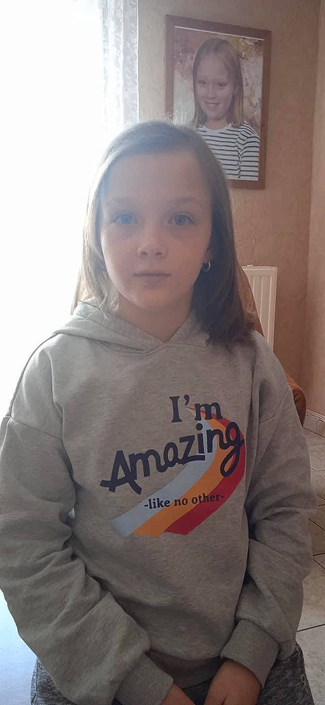 Chloé participe au concours pour gagner de l'argent avec cette photo : brown_hair, cheek, child, chin, cool, forehead, fun, gesture, hair, happy, joy, long_hair, long_sleeved_t_shirt, mouth, neck, nose, person, shoulder, sitting, skin