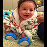 baby, infant, smiling, cozy_clothing, bathrobe, blue_slippers, curly_hair, carpet, indoor, hand_support, happy, cute, child, face, person, home, soft_texture, warm, expression, sitting