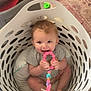 baby, child, laundry_basket, toy, pink, indoor, floor, rug, smiling, happy, seated, clothing, playful, beads, cute, infant, home, person, colorful, candid