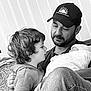 Stevie is registered to the contest to win money with this photo: child, man, beard, cap, curly_hair, couch, indoor, black_and_white, portrait, family, love, tender, seated, casual_clothing, vertical_blinds, closeup, interaction, person, young_child, adult
