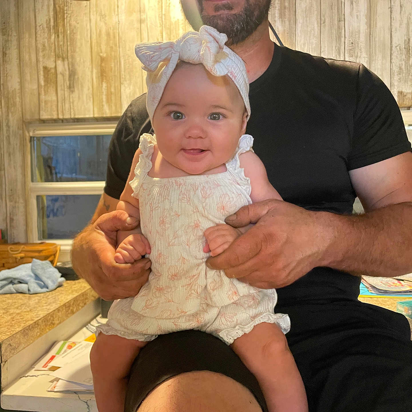 Stevie is registered to the contest to win money with this photo: arm, baby, beard, casual, clothing, counter, face, furniture, hand, happy, headband, holding, indoor, kitchen, man, person, smile, table, window, wooden_wall