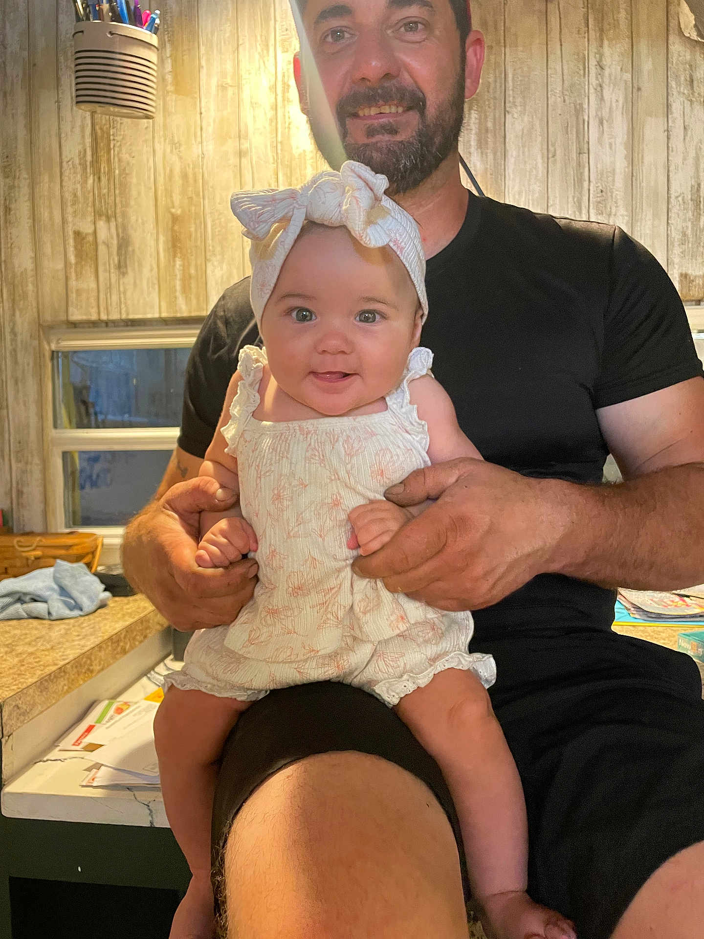 Stevie is registered to the contest to win money with this photo: baby, man, smile, headband, clothing, indoor, kitchen, counter, furniture, person, holding, happy, face, arm, hand, beard, table, wooden_wall, window, casual
