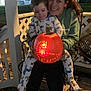 Chase joined the competition — help win amazing prizes! child, woman, pumpkin, glowing, nighttime, pajamas, animal_print, porch, lattice_fence, metal_chair, smiling, holding, outdoor, family, jack_o_lantern, happy, casual_clothing, seated, celebration, autumn