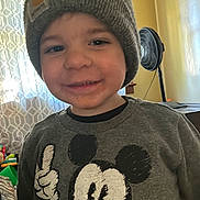 Chase is registered to the contest to win money with this photo: child, toddler, smiling, beanie, gray_sweater, mickey_mouse, indoor, fan, curtains, window, furniture, face, person, clothing, happy, portrait, casual, cozy, home, cute