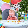 Sylas is registered to the contest to win money with this photo: baby, birthday, high_chair, balloons, party_hat, snacks, outdoor, greenery, capri_sun, decorations, farm_theme, banner, child, smiling, celebration, food, drink, grass, tree, sunny