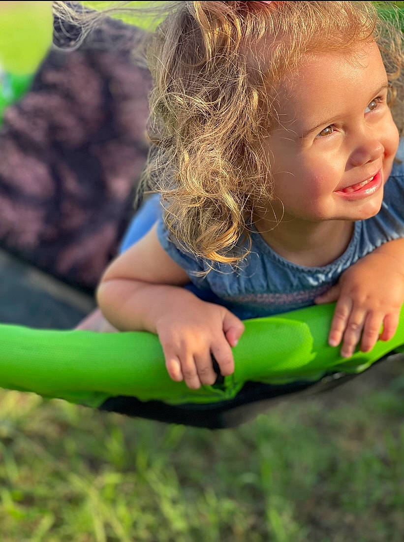 Brynlee is registered to the contest to win money with this photo: child, face, finger, fun, grass, happy, human_leg, joy, lawn, leisure, outdoor_play_equipment, people_in_nature, person, play, recreation, sitting, smile, soil, swing, tableware
